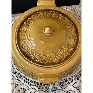 May include: A brown ceramic casserole dish with a lid. The dish has a floral design and a knob on the lid.