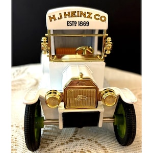 May include: White toy model of a vintage Ford Model T delivery truck with gold accents. The truck has a sign on the top that reads "H.J. Heinz Co. Est. 1869".