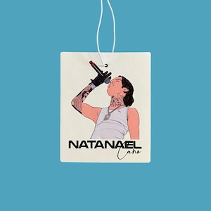 May include: A white car air freshener with a black and white illustration of a man singing into a microphone. The text "NATANAEL Cano" is printed below the illustration.