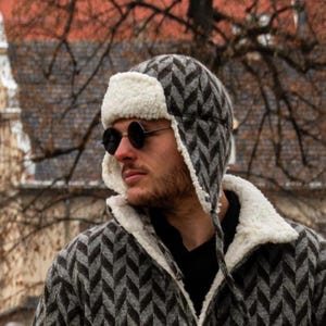 May include: A black and grey chevron patterned trapper hat with a white faux fur trim and ear flaps. The hat has a black strap with a buckle.