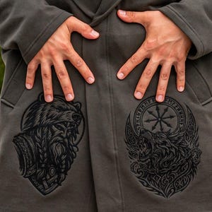 May include: A dark gray hooded coat with two large black graphic designs on the front. One design is a bear's head, and the other is a wolf's head with a circular emblem. The coat has a relaxed fit and a hood.