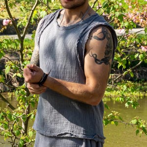 Könnte beinhalten: Ein graues ärmelloses Oberteil und passende Shorts aus einem strukturierten Stoff. Das Oberteil hat einen runden Ausschnitt und einen rohen Saum. Die Shorts haben einen ähnlichen rohen Saum. Das Outfit wird im Freien in der Nähe eines Gewässers und Grünflächen getragen.