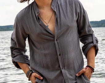 May include: A gray linen shirt with a mandarin collar and long sleeves, buttoned halfway down. The sleeves are rolled up, and the shirt is paired with matching gray pants. A silver necklace with a cross pendant is visible.
