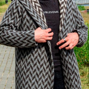 May include: A hooded, long-sleeved coat with a gray and black chevron pattern. The coat is open, revealing a black t-shirt with the word "UBLESOME" printed on it. The coat appears to be made of a thick, warm material.