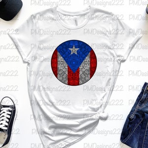 May include: White t-shirt with a circular design of the Puerto Rican flag. The flag is red, white, and blue with a star in the upper left corner. The design is surrounded by a gray and white pattern.