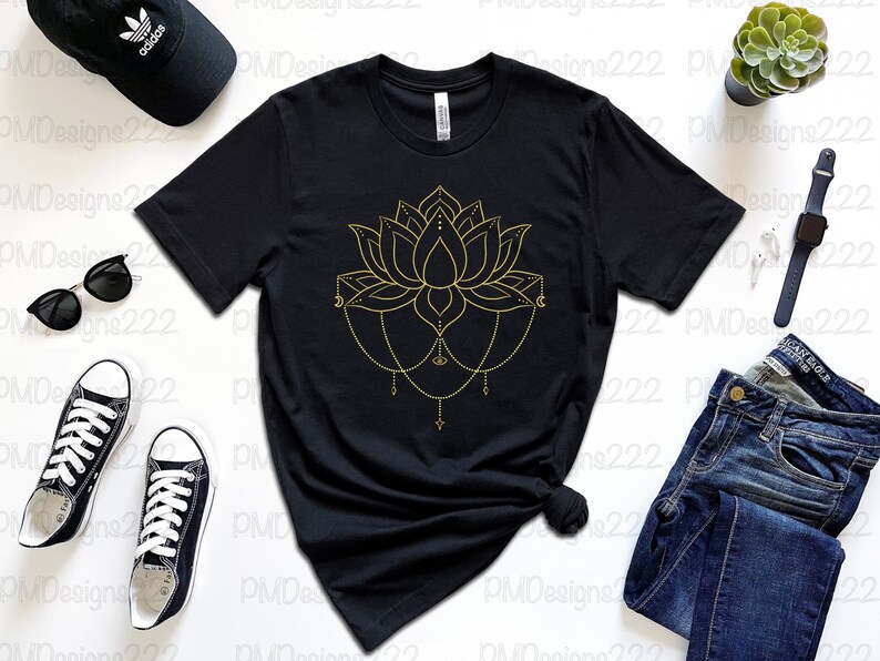 Puede incluir: Camiseta negra con un dise&ntilde;o de flor de loto dorada. El gr&aacute;fico floral presenta detalles intrincados y detalles de cadena colgante. La camiseta se combina con gafas de sol, una gorra negra, zapatillas deportivas y vaqueros.