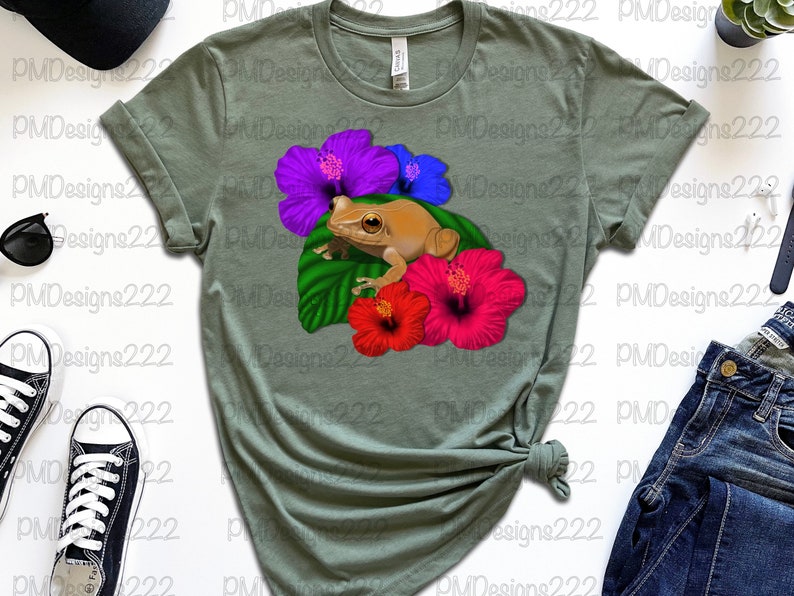 May include: A green t-shirt featuring a brown frog sitting on a green leaf with pink, purple and blue hibiscus flowers.