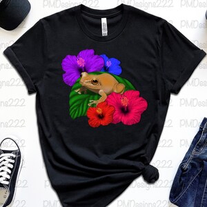 May include: Black t-shirt featuring a graphic of a brown frog sitting on a green leaf with pink, purple and blue hibiscus flowers.