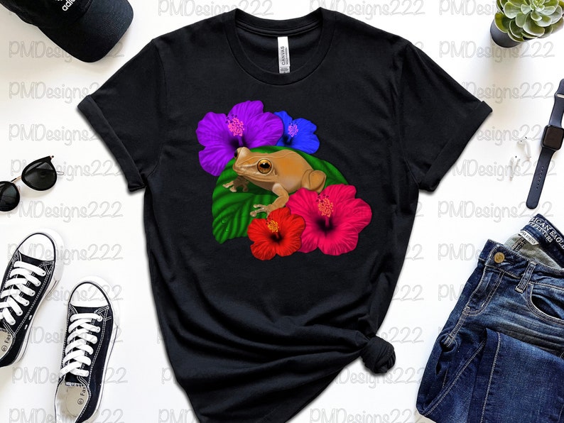 May include: Black t-shirt featuring a graphic of a brown frog sitting on a green leaf with pink, purple and blue hibiscus flowers.