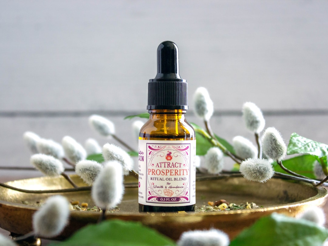 Prosperity ritual oil bottle surrounded by herbs and cotton flowers