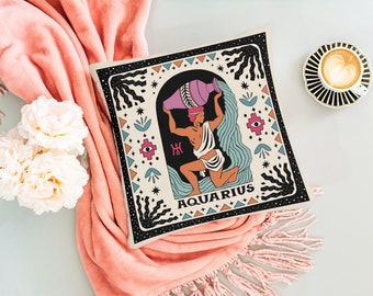 May include: A decorative pillow with a black and white border and a colorful illustration of the astrological sign Aquarius. The illustration features a person pouring water from a pitcher. The pillow has the text "Aquarius" in a black font.