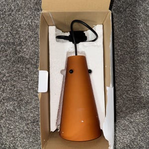 May include: A brown, cone-shaped pendant light fixture with a black cord and mounting hardware, packaged in a cardboard box with white foam inserts. The light fixture has two small black rivets.