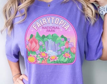 May include: Purple oversized t-shirt with a graphic of a pink and green nature scene with a waterfall and the text "Fairytopia National Park".