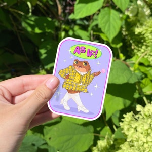 May include: A purple sticker with a cartoon frog wearing a yellow and black plaid outfit and white boots. The frog is holding a pink bubble and the sticker says "AS IF!" in pink letters.