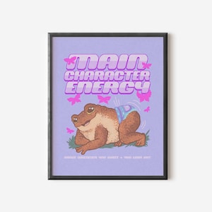 May include: A purple poster with the text "Main Character Energy" in pink letters. A cartoon frog wearing a nappy is in the centre of the poster. The frog is surrounded by pink butterflies. The text "Dance whenever you want + you look hot" is at the bottom of the poster.