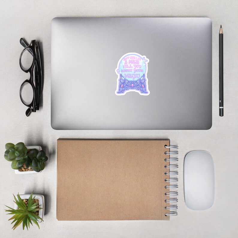 May include: A sticker featuring a crystal ball design with the text "I can and I will tell you about your magic". The crystal ball is light blue and purple, with a decorative base. The sticker is on a laptop.