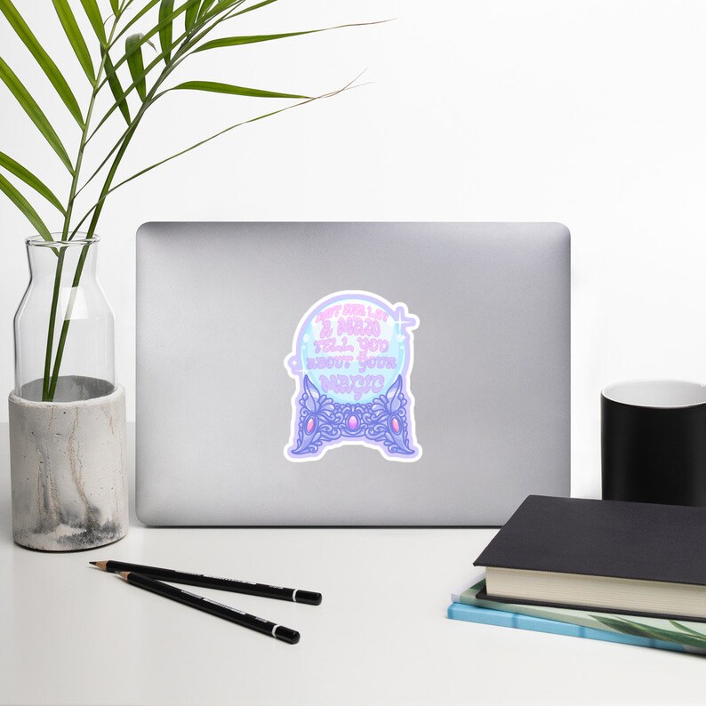 May include: A sticker featuring a crystal ball design with the text "Don't let me tell you about your magic" in a light blue and purple color scheme. The sticker is on a laptop.