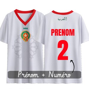 Peut inclure: Maillot de football blanc avec un col en V rouge et un écusson marocain vert et rouge sur le devant. Le dos du maillot porte le mot "PRENOM" et le numéro "2" en rouge.