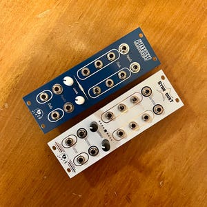 May include: Two synthesizer modules, one blue and one white, with knobs and jacks. The blue module is labeled "Stardust" and the white module is labeled "Star Dust".