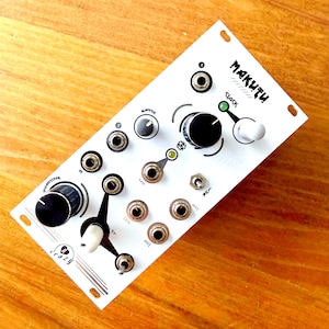 May include: A white electronic music synthesizer module with the word "MAKUTU" in black script. It features numerous knobs, switches, and input jacks. The module has a black and white color scheme with the word "crazy" in a stylized font.
