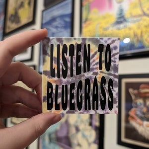 May include: A tie-dye sticker with the text "LISTEN TO BLUEGRASS" in black lettering.