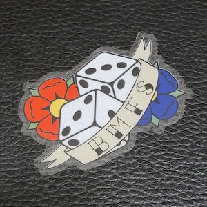 May include: A white sticker with two dice and a banner that says "B.M.I.E.S." The dice are surrounded by a red flower and a blue flower.