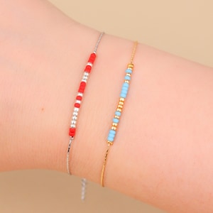 Op de afbeelding: Twee kralenarmbanden om een pols. Een armband is zilver met rode kralen en de andere is goud met lichtblauwe kralen.