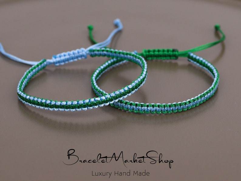 May include: Two friendship bracelets, one blue and green, the other green and blue, are knotted together. The bracelets are made with a woven pattern and have a simple knot closure.