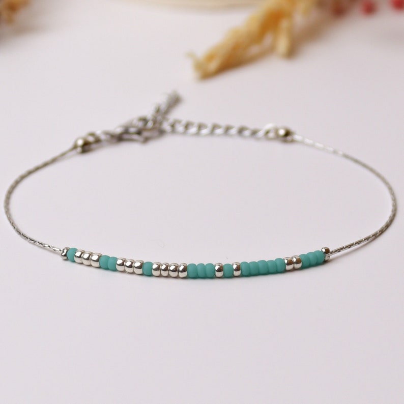 May include: A delicate silver chain bracelet with a row of small turquoise blue beads.