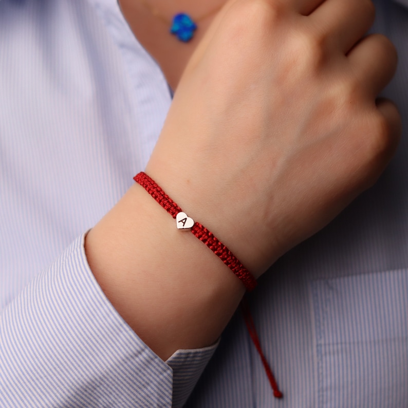 Pode incluir: Pulseira de cord&atilde;o vermelho com um berloque de cora&ccedil;&atilde;o prateado com a letra 'A'.