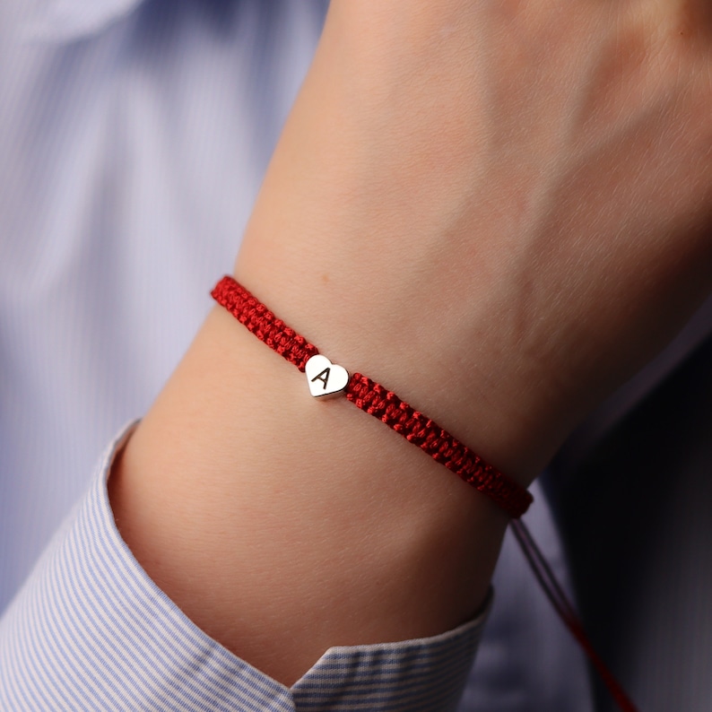 Pode incluir: Um bracelete de corda vermelha com um fecho de cora&ccedil;&atilde;o de prata gravado com a letra "A".
