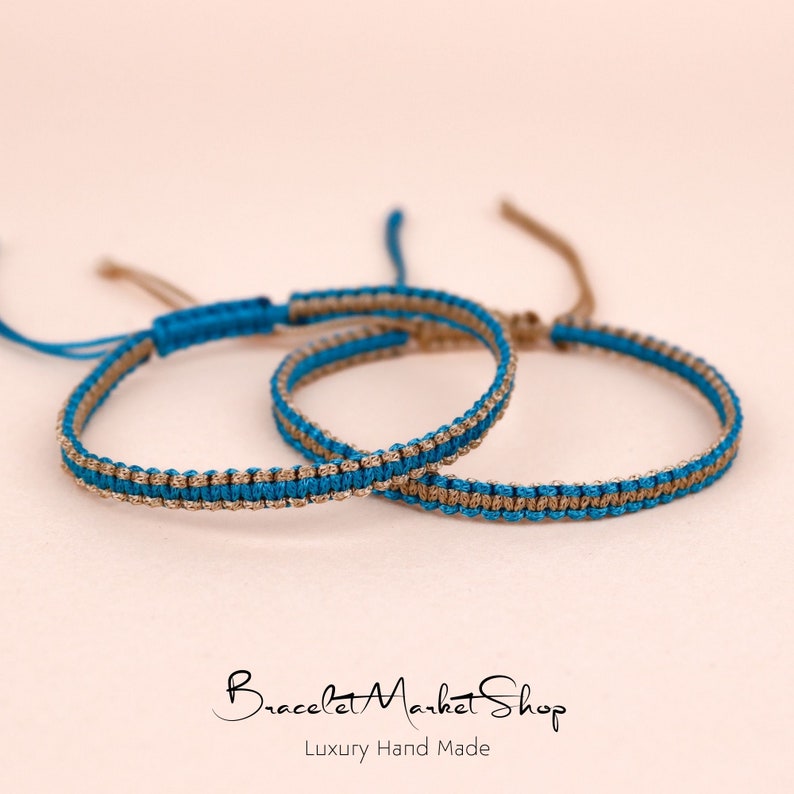 May include: Two friendship bracelets, one blue and one brown, are woven together. The bracelets are made with a simple, elegant design and are perfect for a gift.