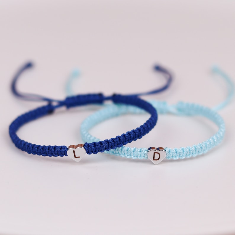 Pode incluir: Duas pulseiras de amizade com pingentes em forma de cora&ccedil;&atilde;o. Uma pulseira &eacute; azul e a outra &eacute; azul claro. A pulseira azul tem a letra "L" no pingente e a pulseira azul claro tem a letra "D" no pingente.