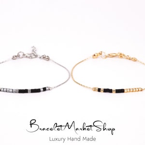 Puede incluir: Dos pulseras delicadas con cuentas negras y plateadas en una cadena plateada y cuentas negras y doradas en una cadena dorada. Las pulseras están sobre un fondo blanco. "Bracelet Market Shop" y "Luxury Hand Made" están escritos debajo de las pulseras.