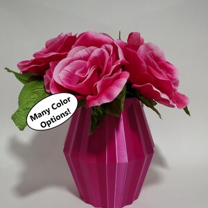 May include: A pink vase with a geometric design holds a bouquet of pink silk roses. The vase is 3D printed and has a glossy finish. A sticker on the vase reads "Many Color Options!"