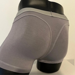 May include: Gray boxer briefs with a light gray waistband and white stitching details. The underwear is displayed on a black mannequin. The fabric appears to be soft and comfortable.