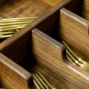 Close up detail shop of silverware reliefs in a walnut drawer organizer. Gold forks pictured.