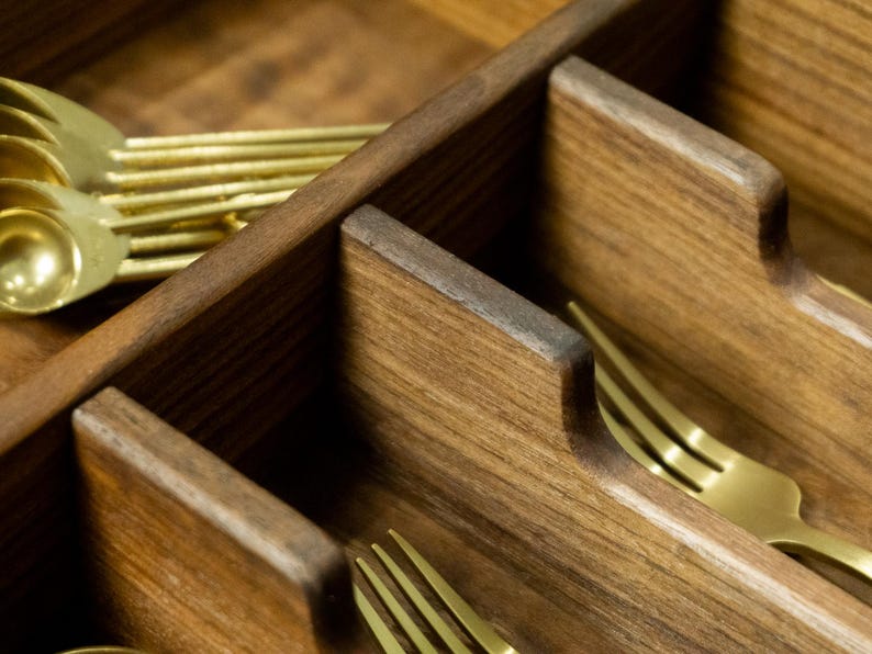 Close up detail shop of silverware reliefs in a walnut drawer organizer. Gold forks pictured.