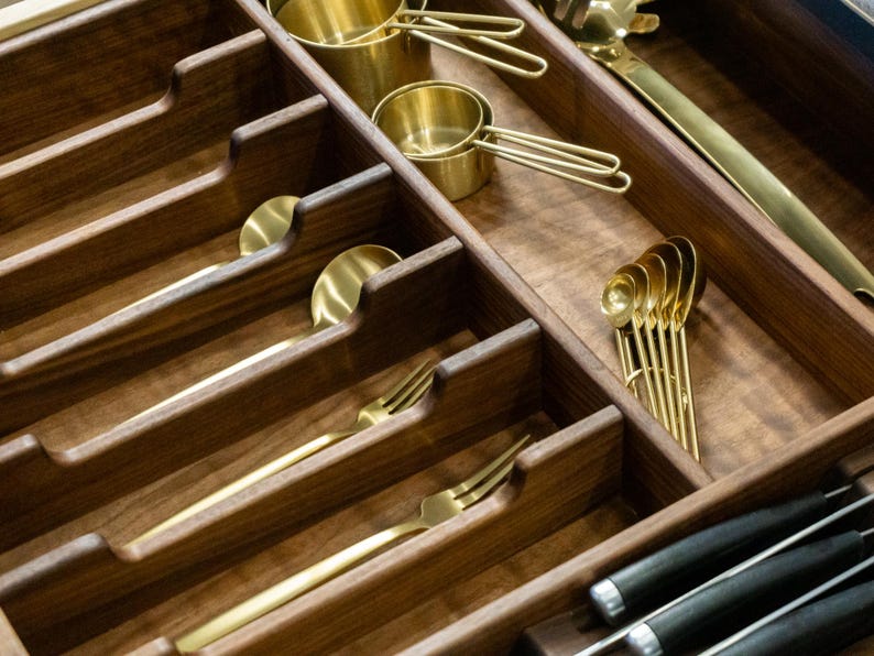 Detail shot highlighting walnut drawer organize silverware reliefs. Neatly organized gold / brass silverware and measuring cups.