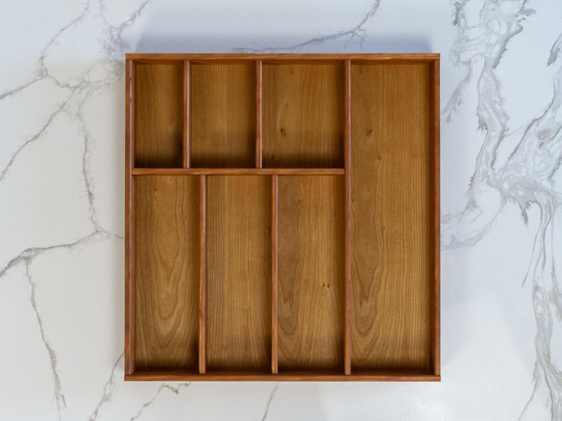 Cherry drawer organizer pictured on marble countertop. Empty, and displaying 7 compartments for cooking utensils.