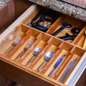 Drawer organizer made in cherry, in drawer. Neatly organized silverware set, and various cooking utensils. Granite countertops pictured.