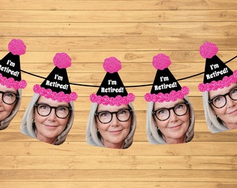 May include: A banner with cutouts of a woman's face wearing glasses, each with a black party hat that reads "I'm Retired!" in white text. The hats have pink glitter pom-poms and trim. The background is a wooden surface.