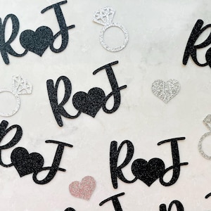Può includere: Ritagli di lettere "R♥J" neri glitterati con cuori e forme di anelli di diamanti argentati su una superficie bianca. Adatto per matrimoni o fidanzamenti.