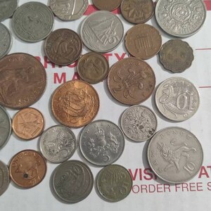 May include: A collection of various coins, including silver, bronze, and copper examples. The coins feature different designs, including portraits, heraldic symbols, and ships. Some coins have visible text, and the collection is arranged on a white surface.