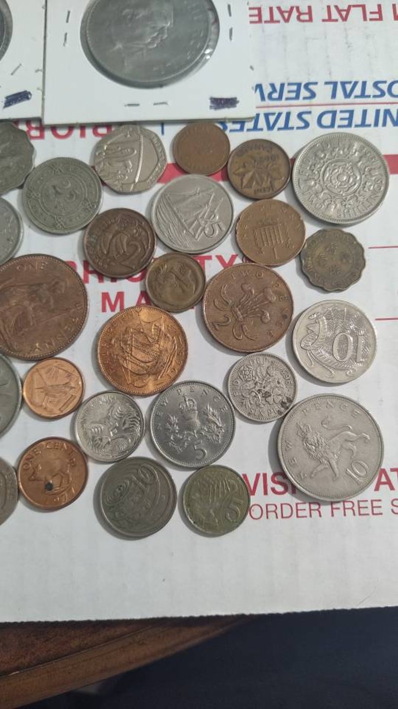 May include: A collection of various coins, including silver, bronze, and copper examples. The coins feature different designs, including portraits, heraldic symbols, and ships. Some coins have visible text, and the collection is arranged on a white surface.