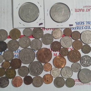May include: A collection of various coins, including silver and copper, scattered on a white surface. Two coins are encased in protective sleeves. The coins vary in size and design, showcasing historical currency.