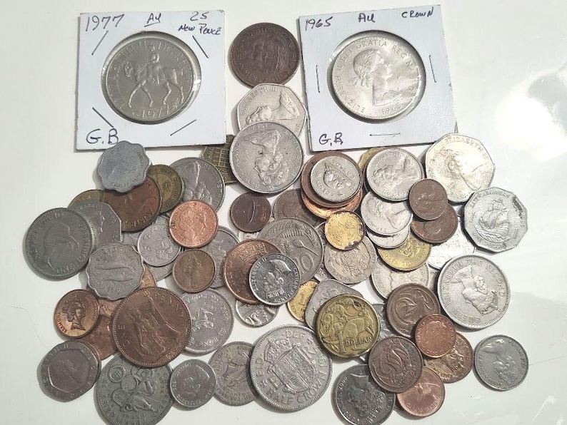 May include: A collection of various coins, including silver and copper pieces. Two coins are in protective holders, one dated 1977 with a horse and rider, and another from 1965. The coins vary in size and design, showcasing historical currency.