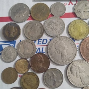 May include: A collection of various coins, including silver and copper-toned pieces. The coins feature profiles and other designs. Some coins are in protective holders, and the text "G.B." is visible.