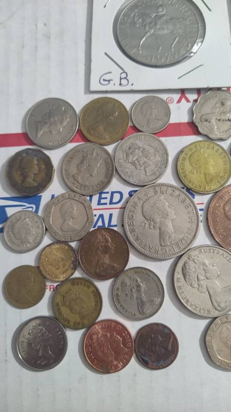 May include: A collection of various coins, including silver and copper-toned pieces. The coins feature profiles and other designs. Some coins are in protective holders, and the text "G.B." is visible.
