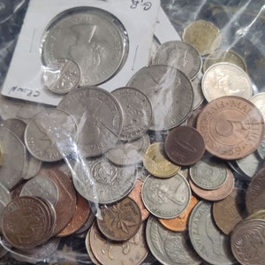 May include: A clear plastic bag filled with a variety of coins. The coins are of different sizes, shapes, and colors, including silver, copper, and bronze. Some coins are partially visible, while others are stacked on top of each other.